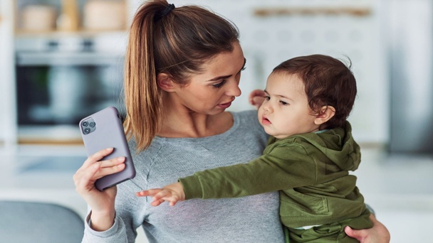 תינוק בזרועות אמו מושיט יד לטלפון אפליקציות לקטנטנים בגיל הרך