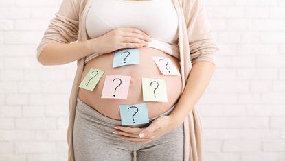 אישה בהריון מבולבלת מול לוח שמות עם סימני שאלה, מתלבטת בבחירת שם מתוך רשימת שמות לבנים – רגע שממחיש את הקושי בהחלטה החשובה.